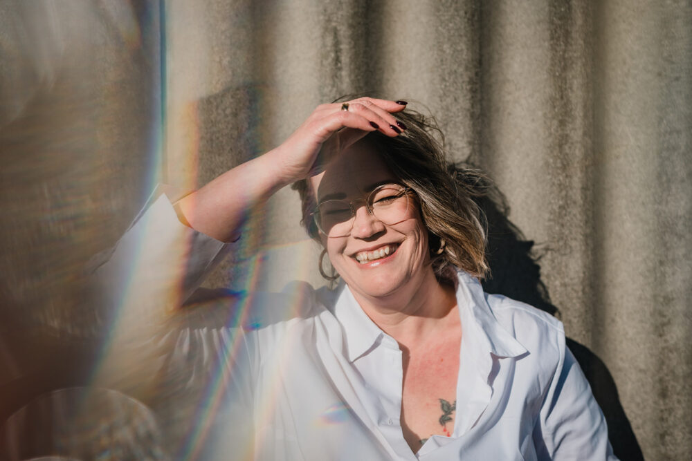 Lächelnde Fotografin hält sich die Hand vor ihr Gesicht, um etwas Schatten zu haben und lächelt glücklich