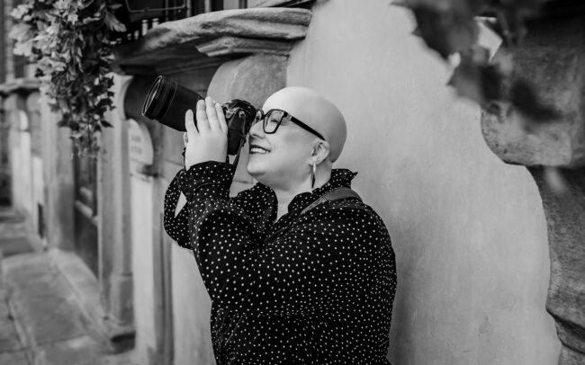 Fotografin lehnt an einer Wand in Florenz und blickt gen Himmel durch ihre Kameralinse